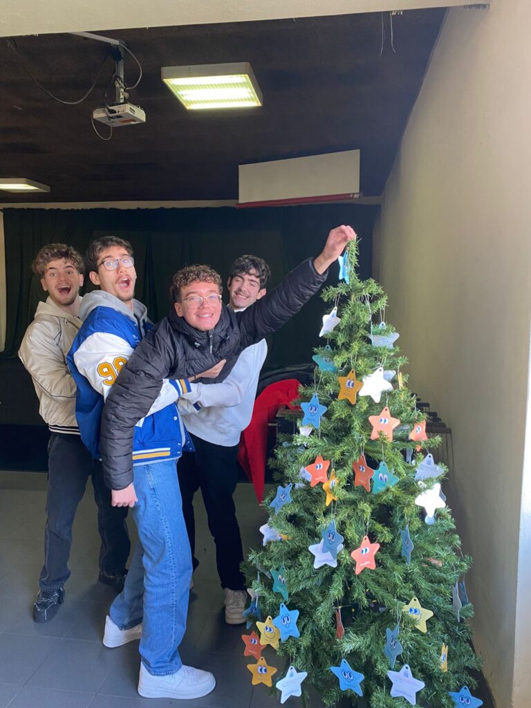 Jovens divertidos em escola com árvore de natal decorada com estrelas de natal Make-A-Wish 2024