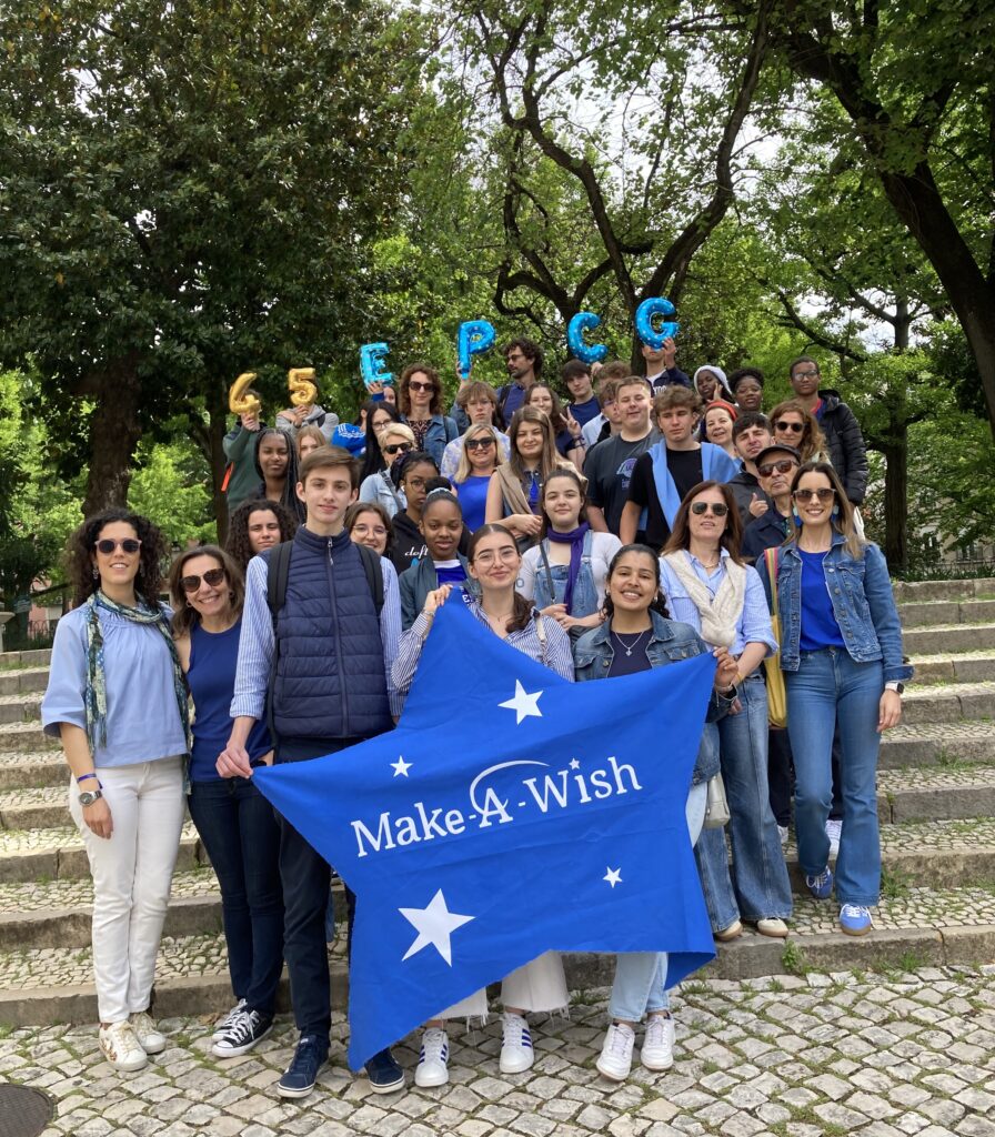 vários adolescentes e professores, numa escadaria, estão a segurarem numa bandeira azul em forma de estrela com o logotipo Make-A-Wish